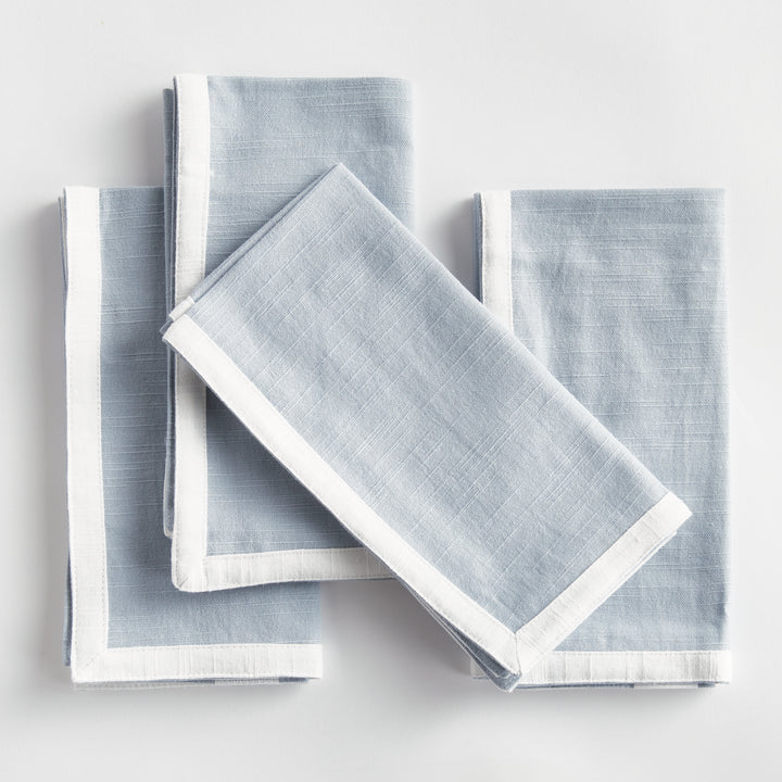 Blue and white dinner napkins, folded in a layered arrangement, showing the border and square cotton fabric. Transitional