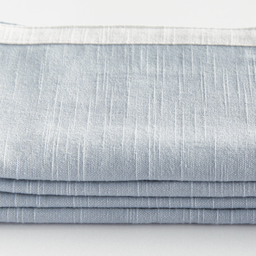 Blue and white dinner napkins, close detail showing the cotton weave and contrasting border above folded fabric. Transitional