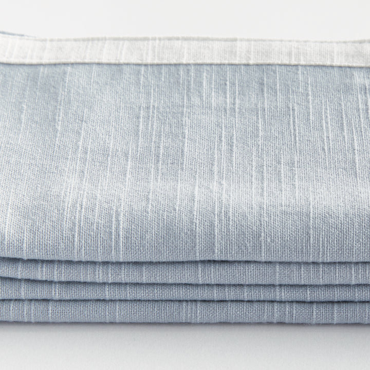 Blue and white dinner napkins, close detail showing the cotton weave and contrasting border above folded fabric. Transitional