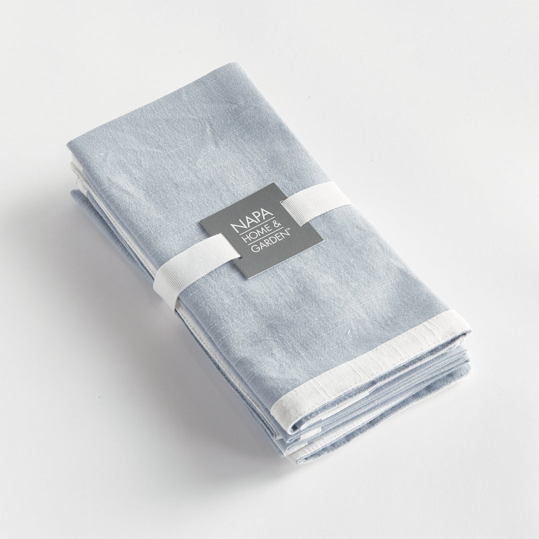 Blue and white dinner napkins, folded as a set tied with a ribbon, showing the border and cotton weave. Classic Transitional