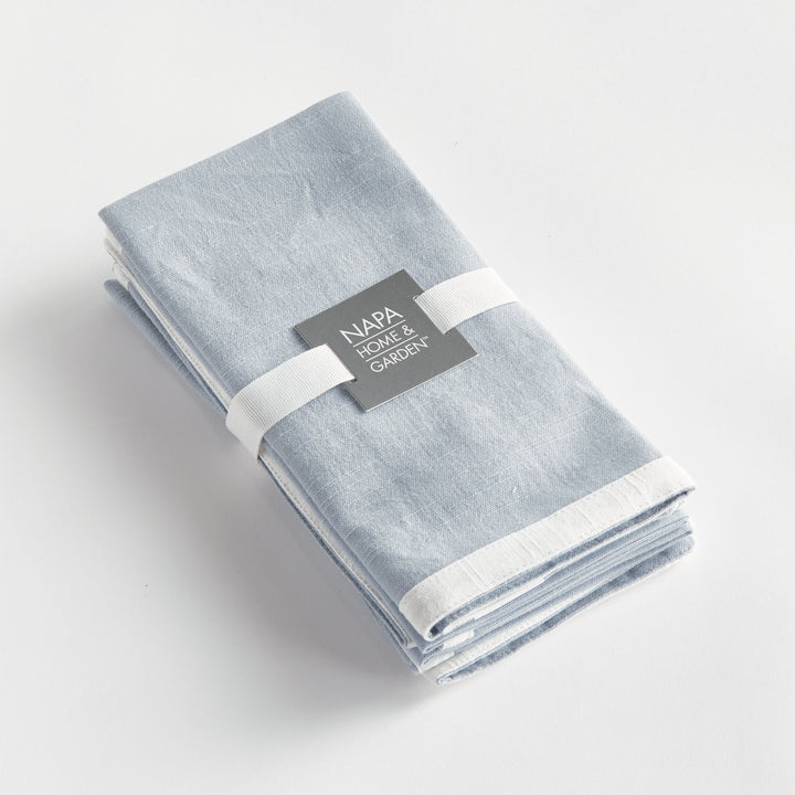 Blue and white dinner napkins, folded as a set tied with a ribbon, showing the border and cotton weave. Classic Transitional