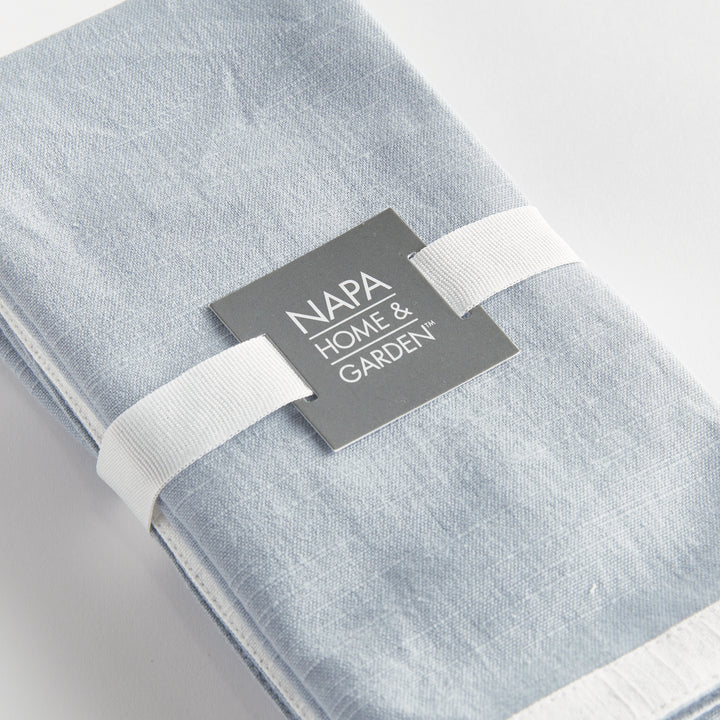 Blue and white dinner napkins, close view of the set tied with ribbon, showing the border and woven surface. Transitional
