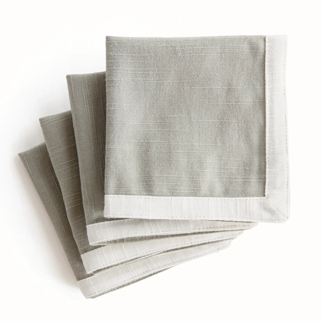 Green and white cocktail napkins, folded as a stack, showing the white border and green woven cotton fabric. Transitional