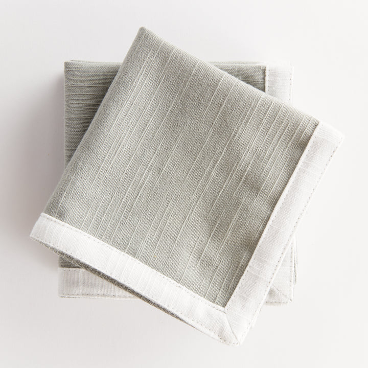 Green and white cocktail napkins, layered and folded, showing green cotton panels framed by white cloth borders. Transitional