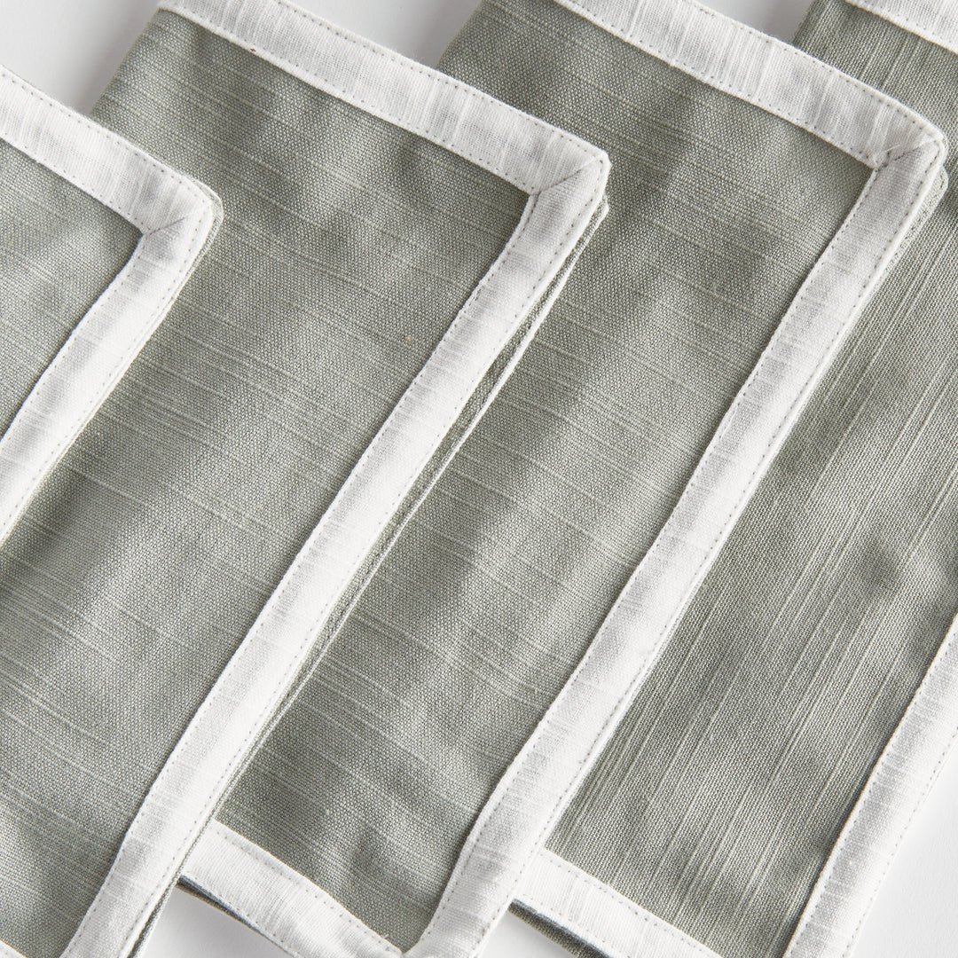 Green and white cocktail napkins, close view showing white cloth borders, woven cotton texture and folded edges. Transitional