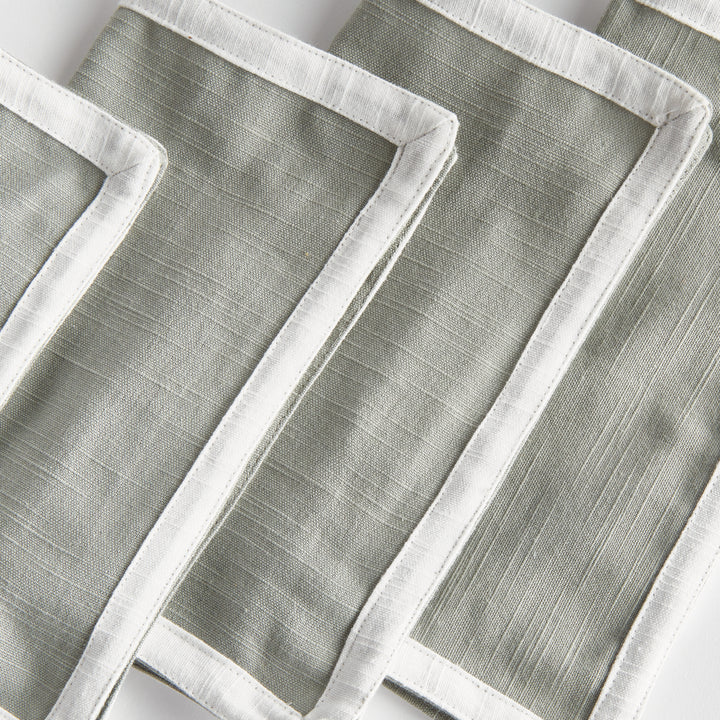 Green and white cocktail napkins, close view showing white cloth borders, woven cotton texture and folded edges. Transitional