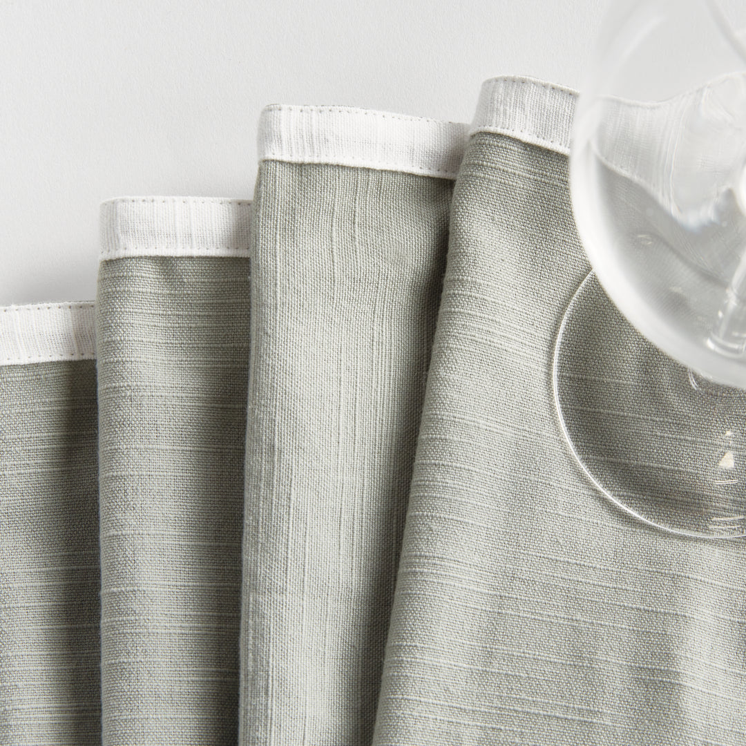 Green and white cocktail napkins, folded beside glasses, showing the white border and soft green cotton surface. Transitional