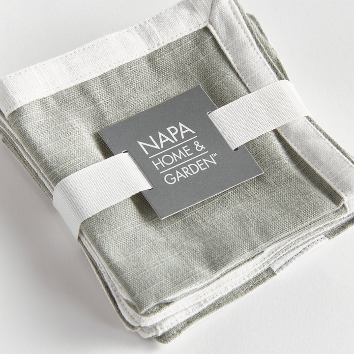 Green and white cocktail napkins, close view of ribbon-tied set, showing white border and woven green cotton. Transitional