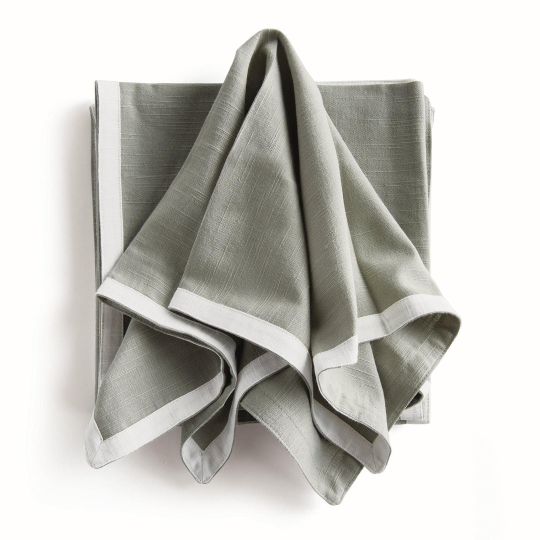 Green and white dinner napkins, draped over a folded stack, showing the contrast border and the cotton texture. Transitional