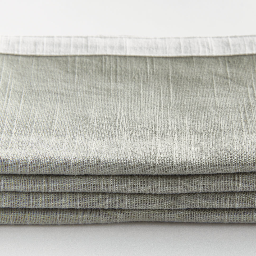 Green and white dinner napkins, close detail showing the cotton weave and border above folded fabric. Classic Transitional