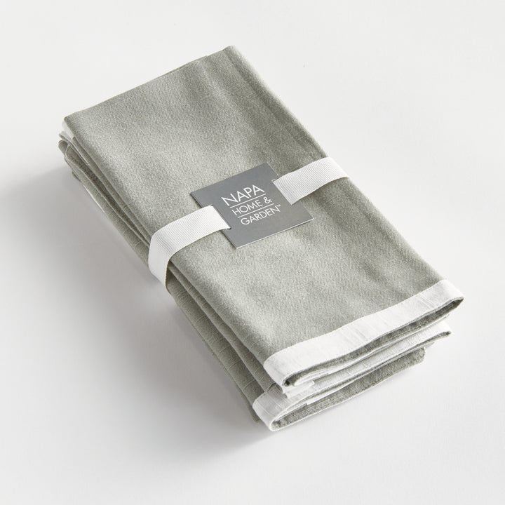 Green and white dinner napkins, folded as a set tied with a ribbon, showing the border and cotton weave. Classic Transitional