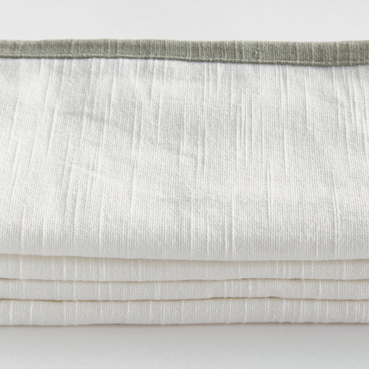 White and sage dinner napkins, close detail showing the cotton weave and contrasting border above folded fabric. Transitional