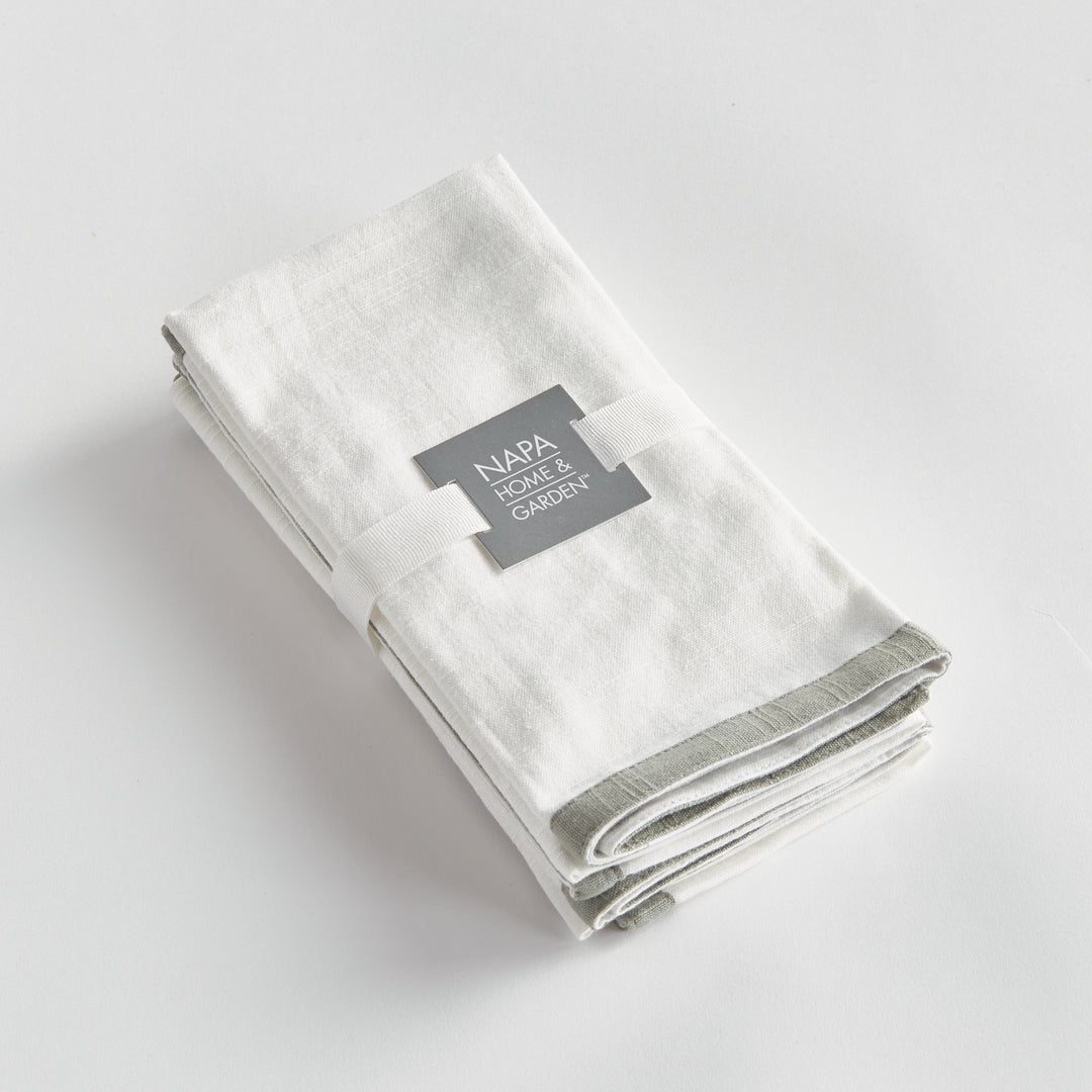 White and sage dinner napkins, folded as a set tied with a ribbon, showing the border and cotton weave. Classic Transitional