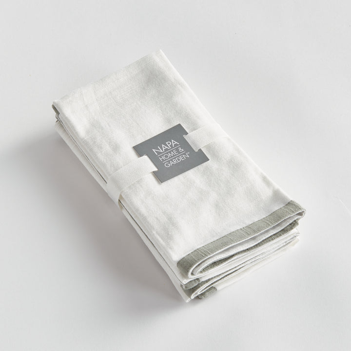 White and sage dinner napkins, folded as a set tied with a ribbon, showing the border and cotton weave. Classic Transitional