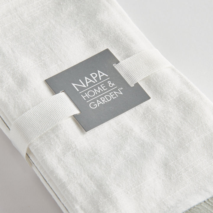 White and sage dinner napkins, close view of the set tied with ribbon, showing the border and woven surface. Transitional