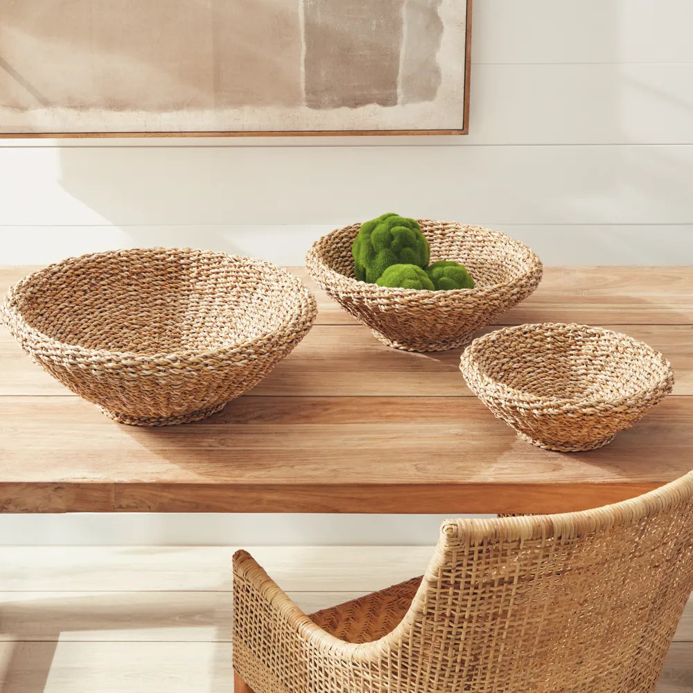 Woven seagrass bowl set styled on a wooden dining table with a rattan chair, bright natural light, coastal farmhouse decor
