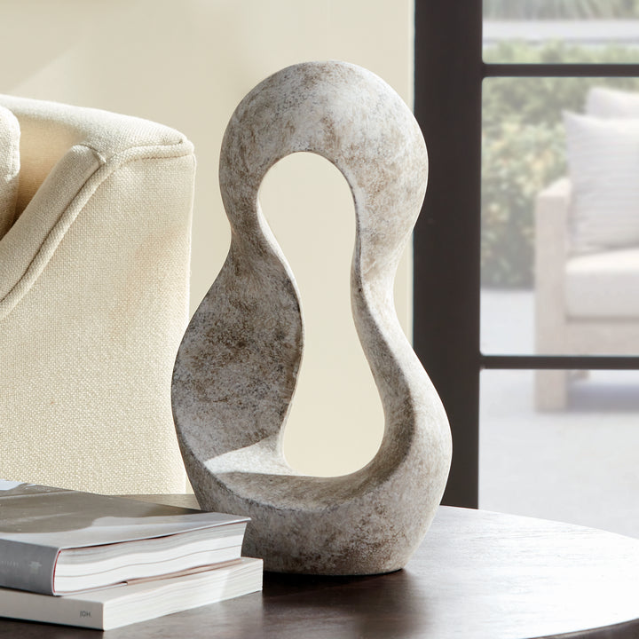 Hand-shaped abstract clay sculpture placed on round tabletop next to books and sofa, showcasing matte earthstone finish and full scale.