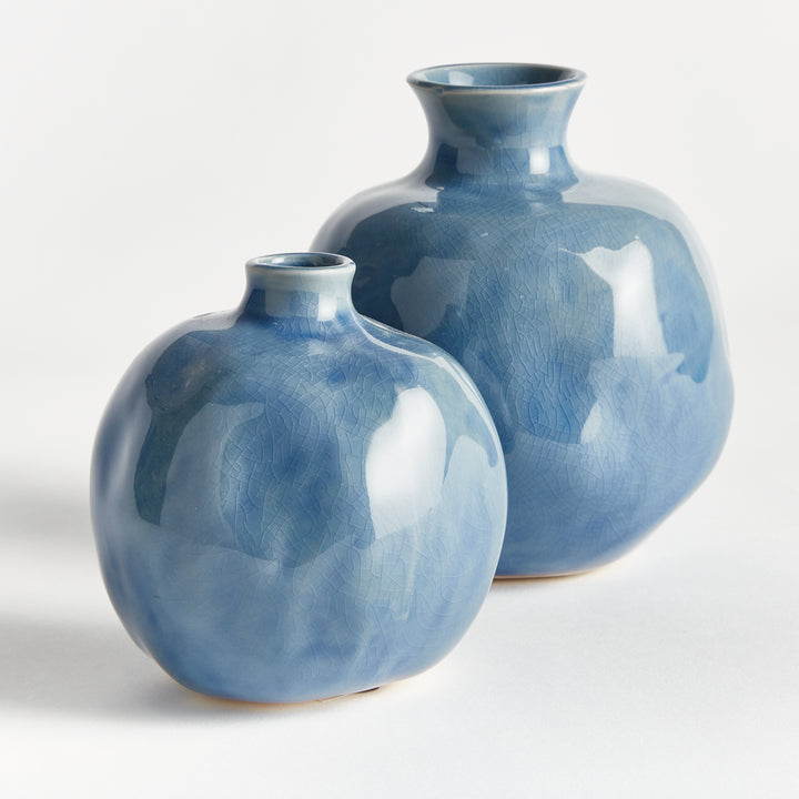 Angled view of two blue ceramic bud vases showing their rounded bodies, short necks and tonal glazed surfaces. Transitional
