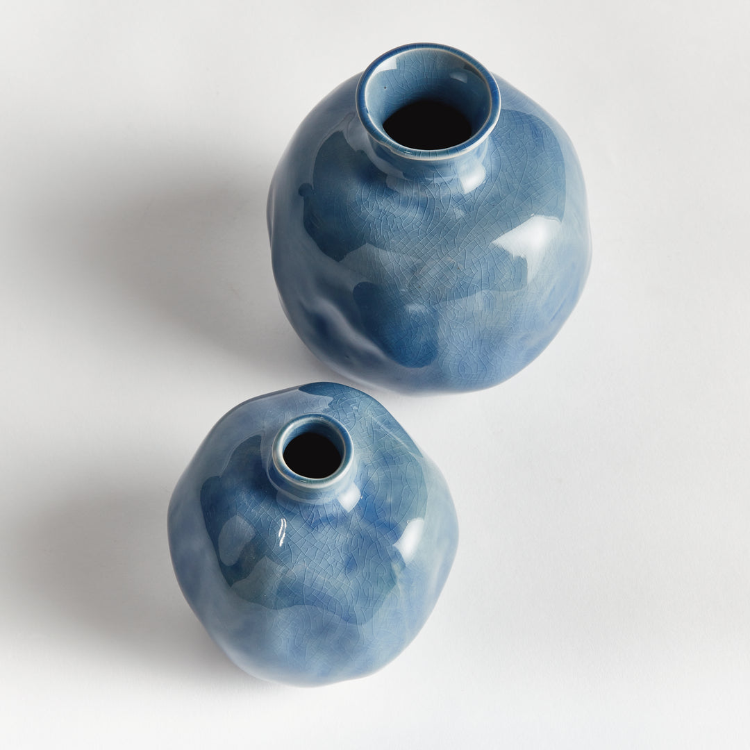 Overhead view of two blue ceramic bud vases showing their narrow openings, necks and rounded glazed bodies. Transitional