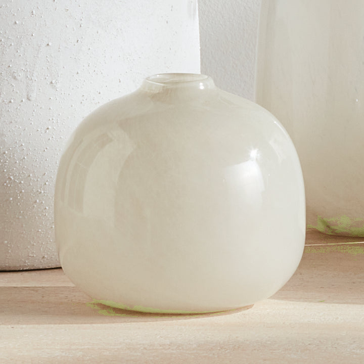 Ivory round glass vase on a pale console, with a taller neutral object behind it and reflected light, Modern Organic style