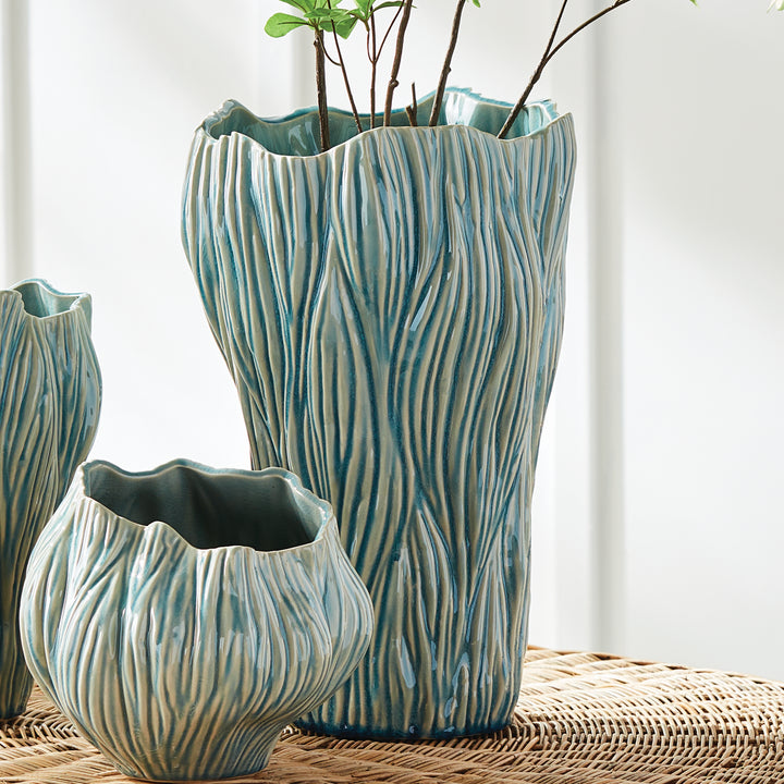 Large blue textured ceramic vase with stems, styled beside smaller coordinating vessels on woven chair, Coastal Transitional
