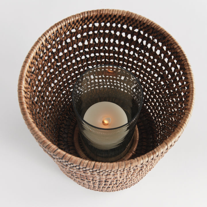 Top view into a large warm brown rattan hurricane showing a candle inside its glass cylinder and woven sides, Transitional