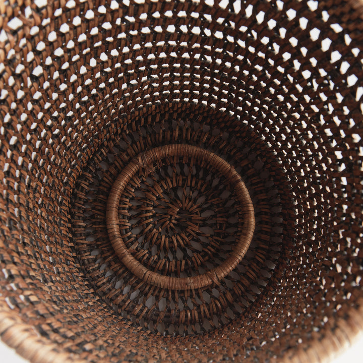 Overhead view into an empty large warm brown rattan hurricane showing the woven base and open cylindrical sides, Transitional