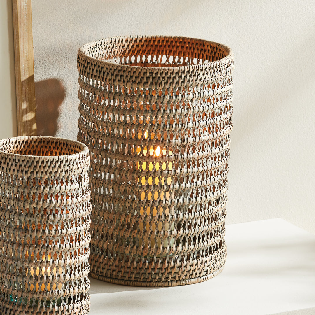 Large warm brown rattan hurricane with candlelight inside, beside a smaller matching hurricane on a console, Transitional