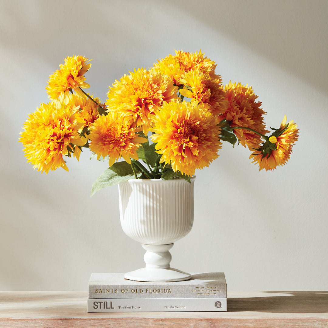 Large white ribbed ceramic footed cachepot holding yellow flowers, displayed on stacked books in an interior, Traditional