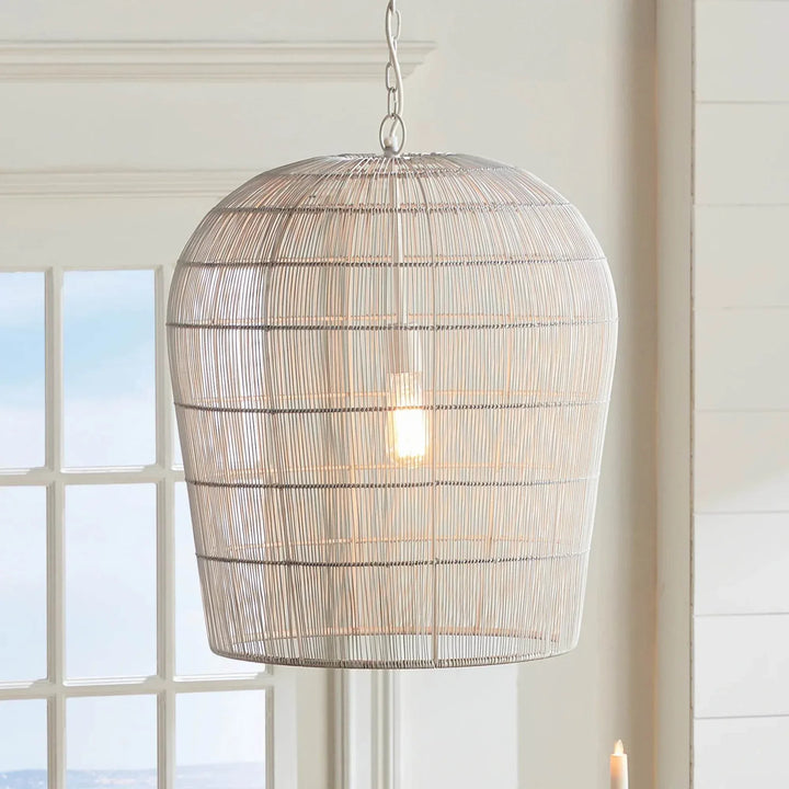Large white woven iron pendant light illuminated near a window, with light showing through the open cage shade, Coastal style