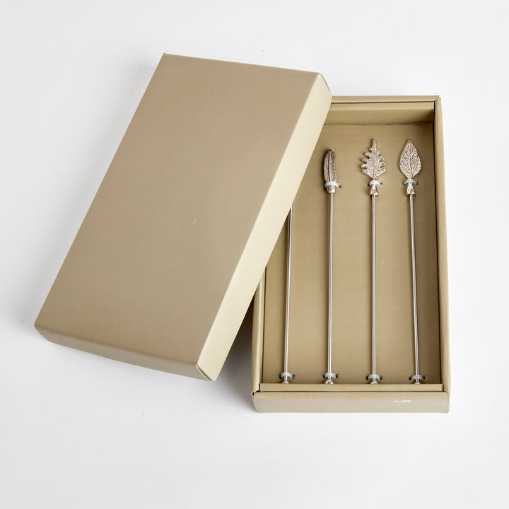Laurel silver leaf swizzle sticks arranged in an open presentation box with the lid beside the set on white. Transitional