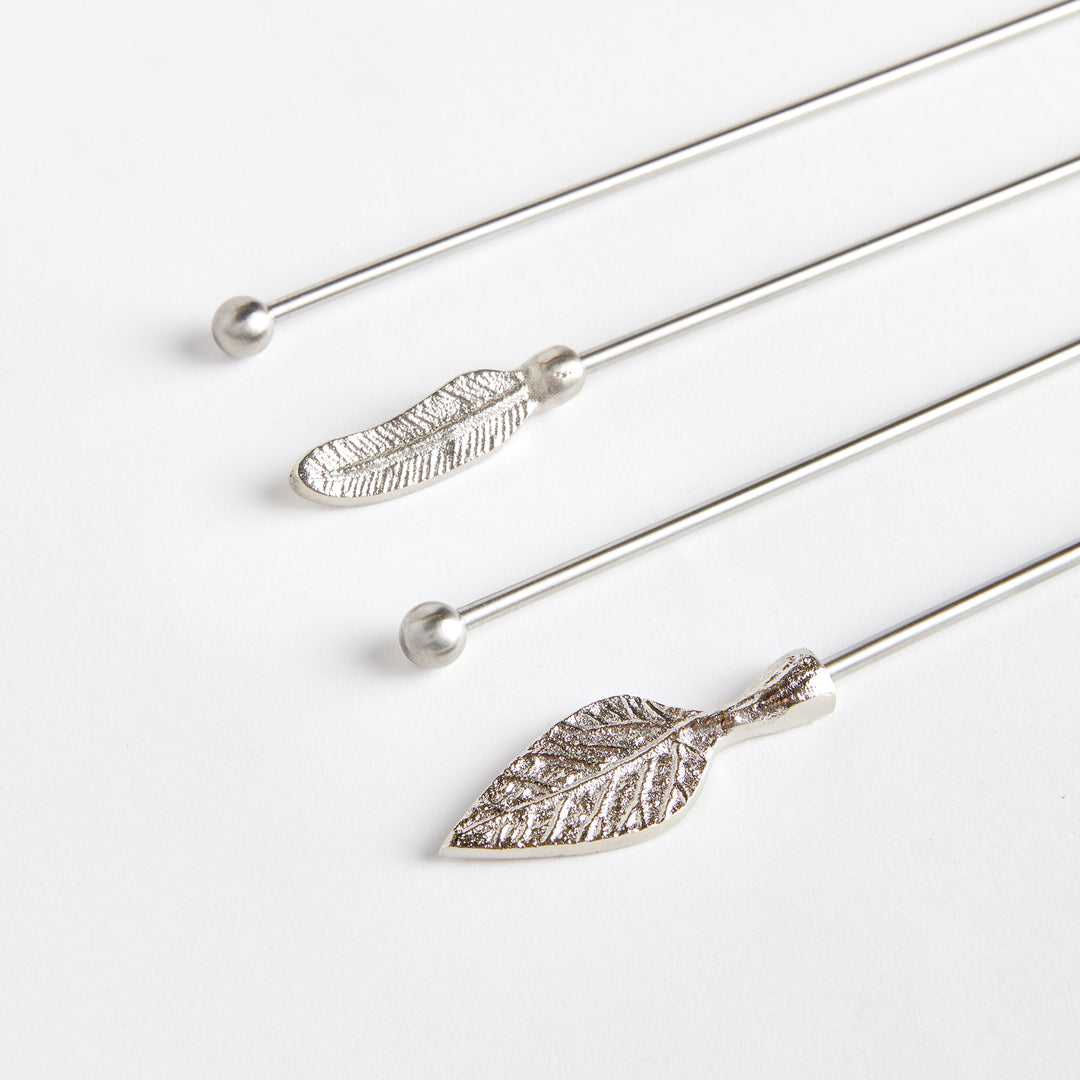 Angled view of Laurel silver stainless steel swizzle sticks showing assorted botanical tops and rounded ends. Transitional