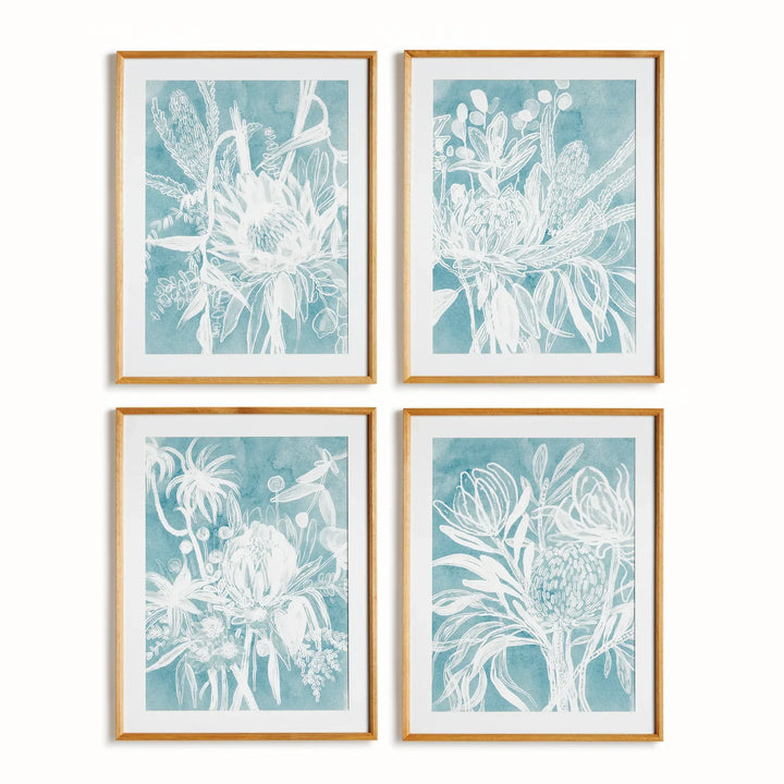 Four blue protea art prints with pale floral illustrations, white mats and natural wood frames, arranged in a grid. Coastal