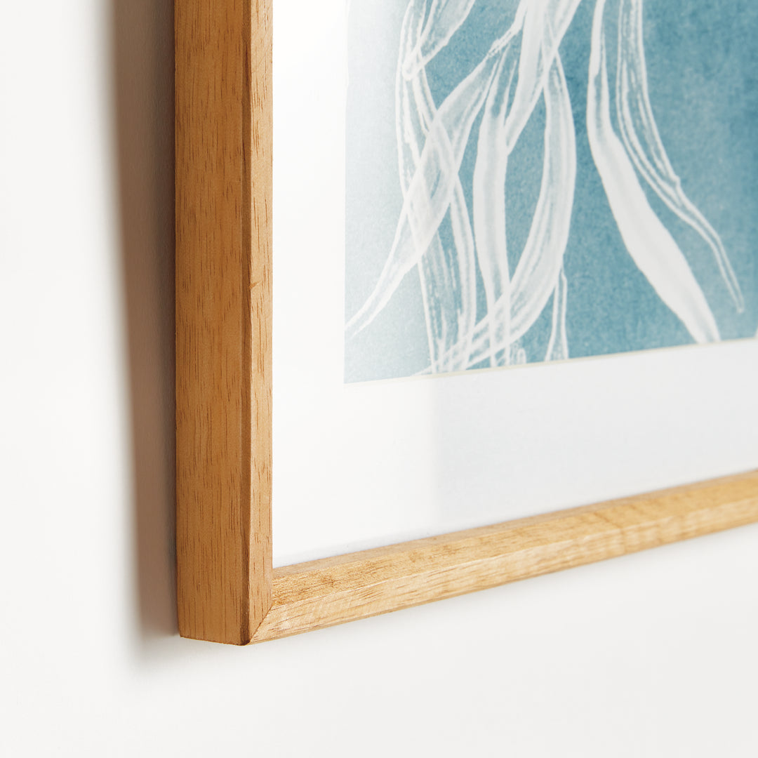 Close view of a blue protea print showing the white mat, natural wood frame and pale botanical lines on blue artwork. Coastal