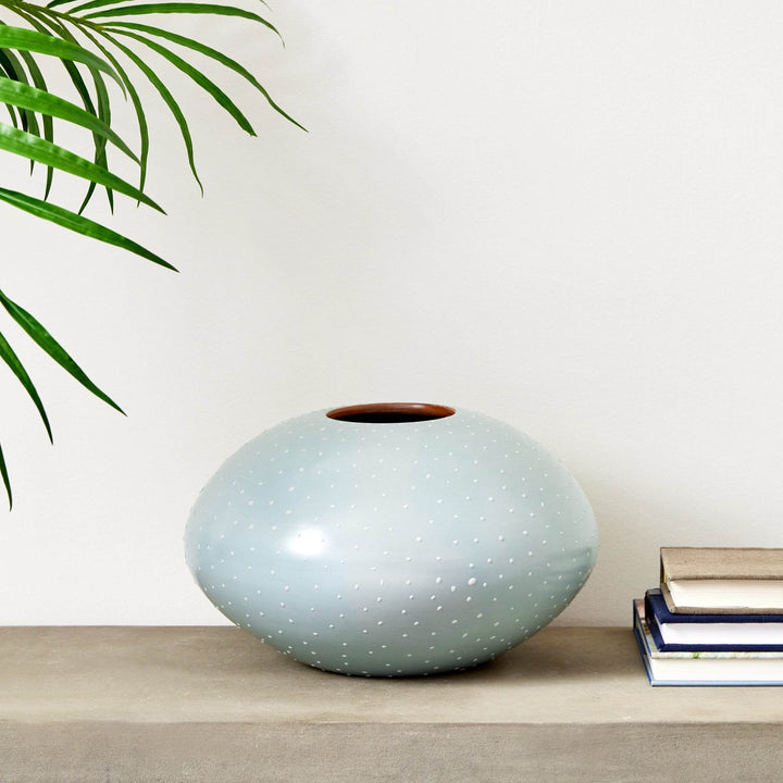 Medium light blue ceramic vase with white stipple detailing shown on a concrete console with stacked books – Modern Organic.


