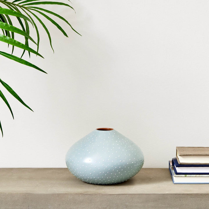 Light blue ceramic vase with white stipple detail displayed on a concrete console beside books and a palm leaf – Modern Organic.


