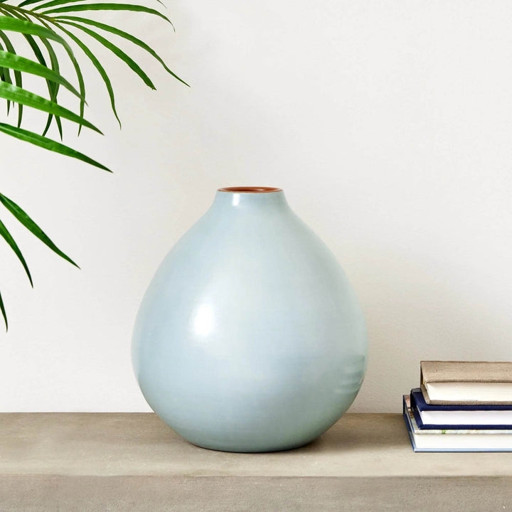 Light blue ceramic vase with round form and narrow neck, styled on a console shelf with books – Modern Organic.