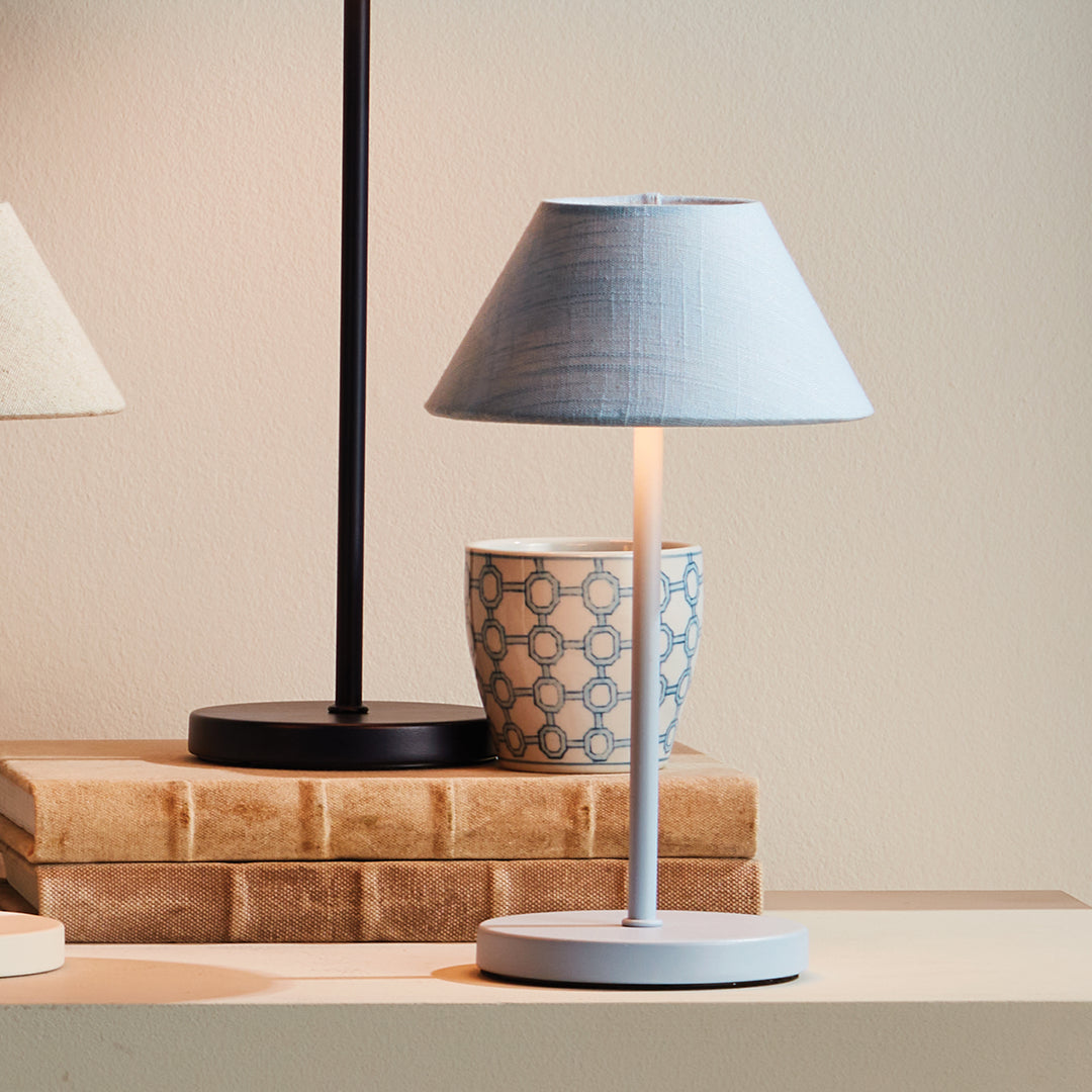 Light blue cordless LED table lamp with linen empire shade styled on a tabletop with decorative accents – Coastal Transitional