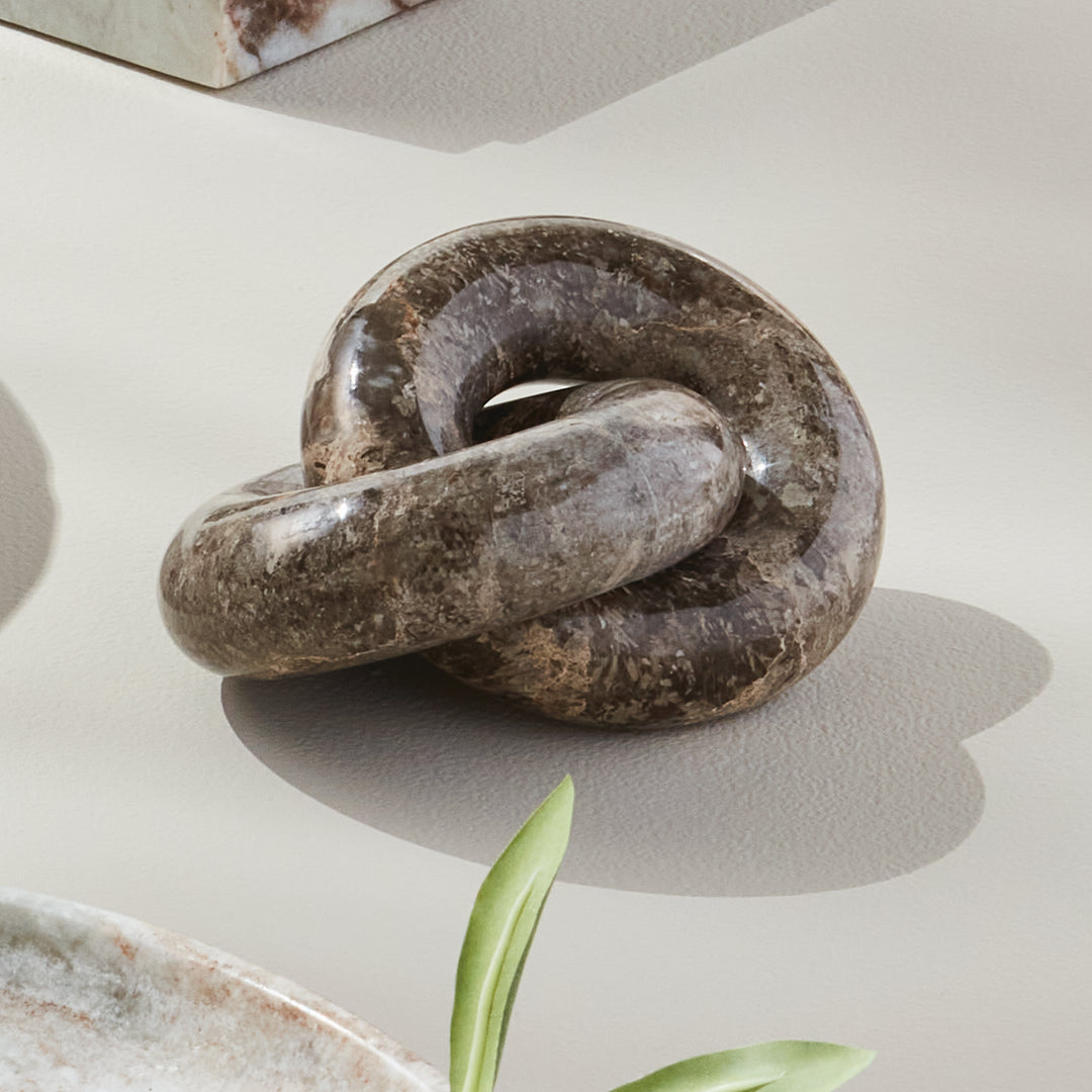 Linked marble rings sculpture styled in sunlight on a pale surface, showing brown veining and curved shadows - Modern Organic
