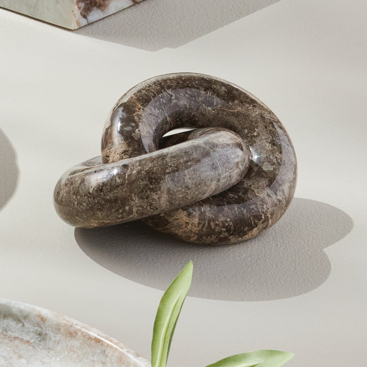Linked marble rings sculpture styled in sunlight on a pale surface, showing brown veining and curved shadows - Modern Organic