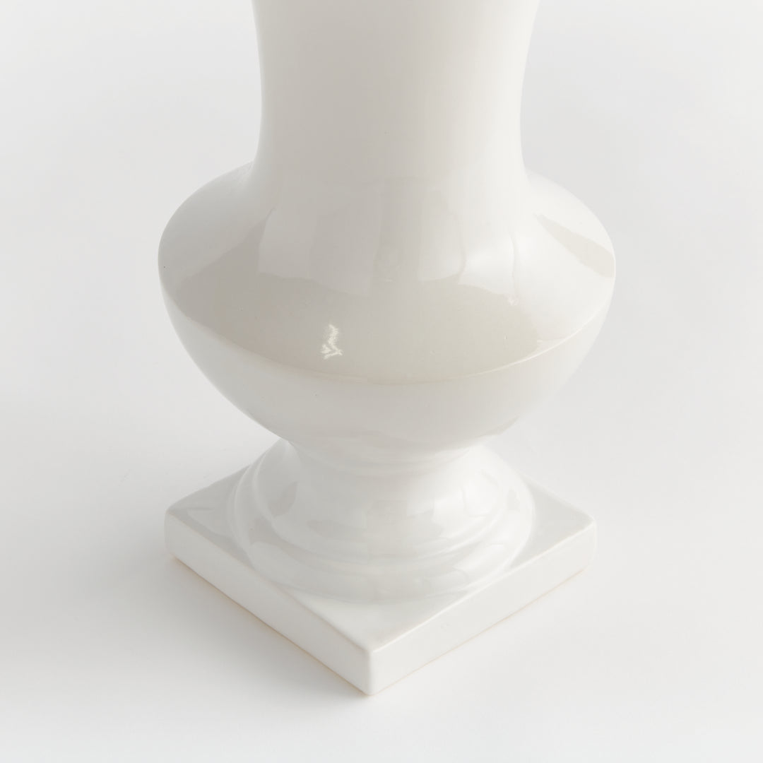 Detail of a large white ceramic footed vase showing its curved body and shaped square pedestal base, in Traditional style