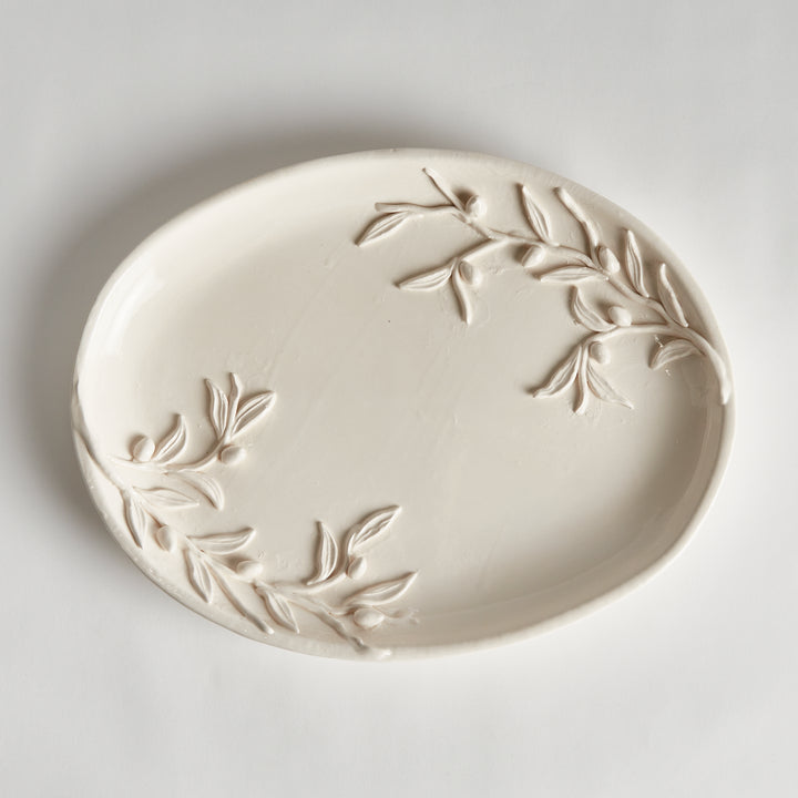 Overhead view of a white oval ceramic tray showing olive branch relief at opposite ends and a gently raised edge. Traditional