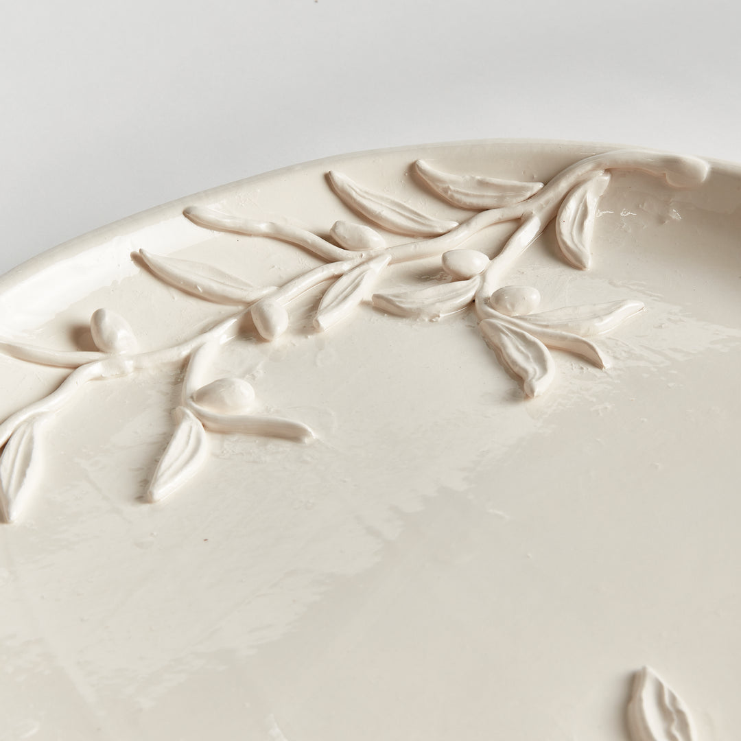 Close detail of handmade olive branches, leaves and fruit applied across a white glazed Italian decorative tray. Traditional