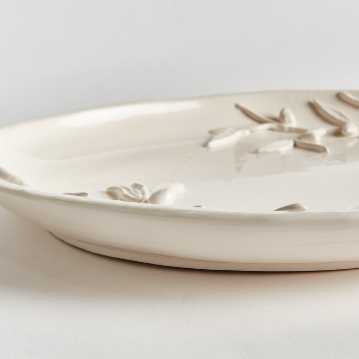 Side detail of a white oval ceramic decorative tray showing a shallow curved rim and raised olive branch detail. Traditional