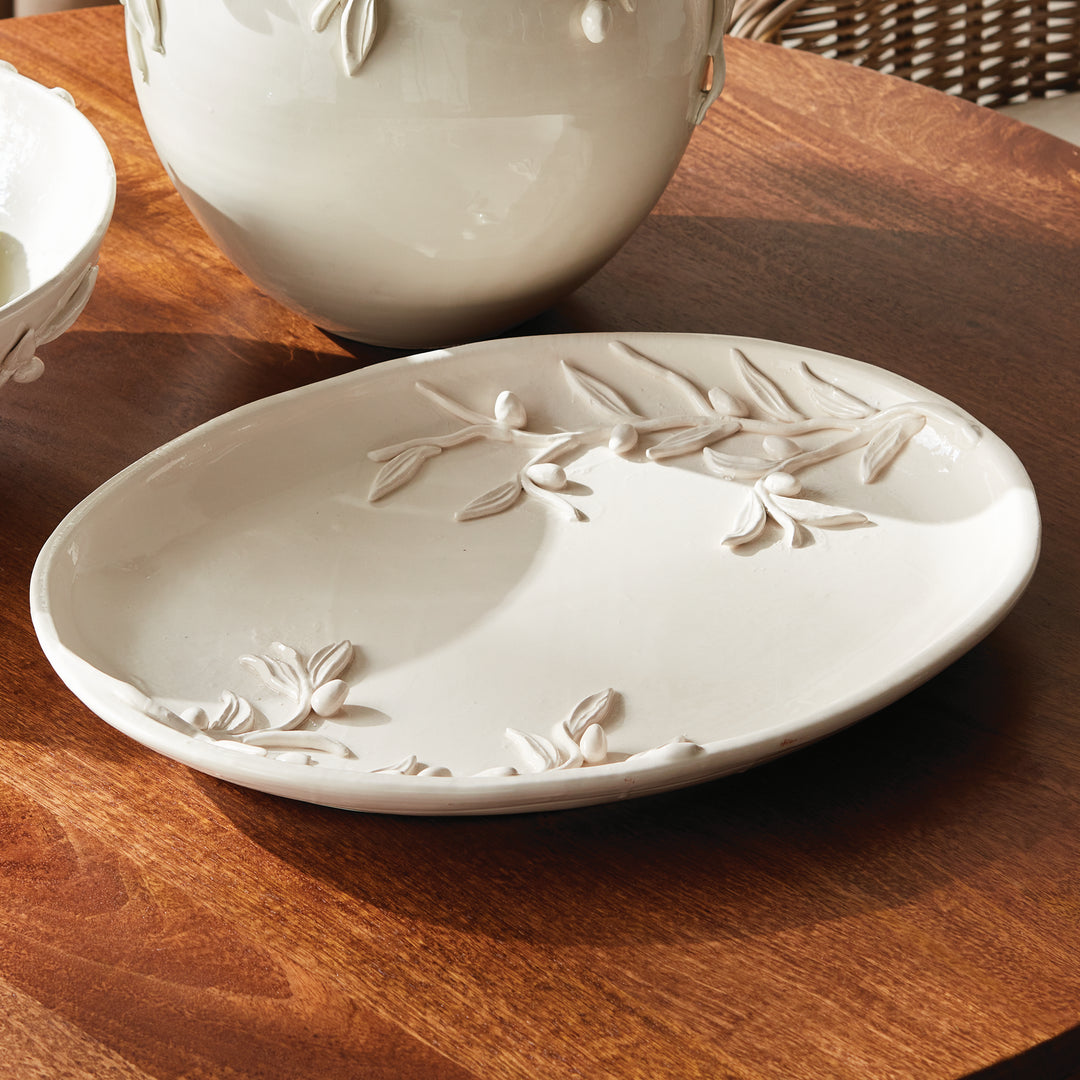 White olive relief tray on a wood table beside the coordinating rounded vase, showing its oval glazed surface. Traditional
