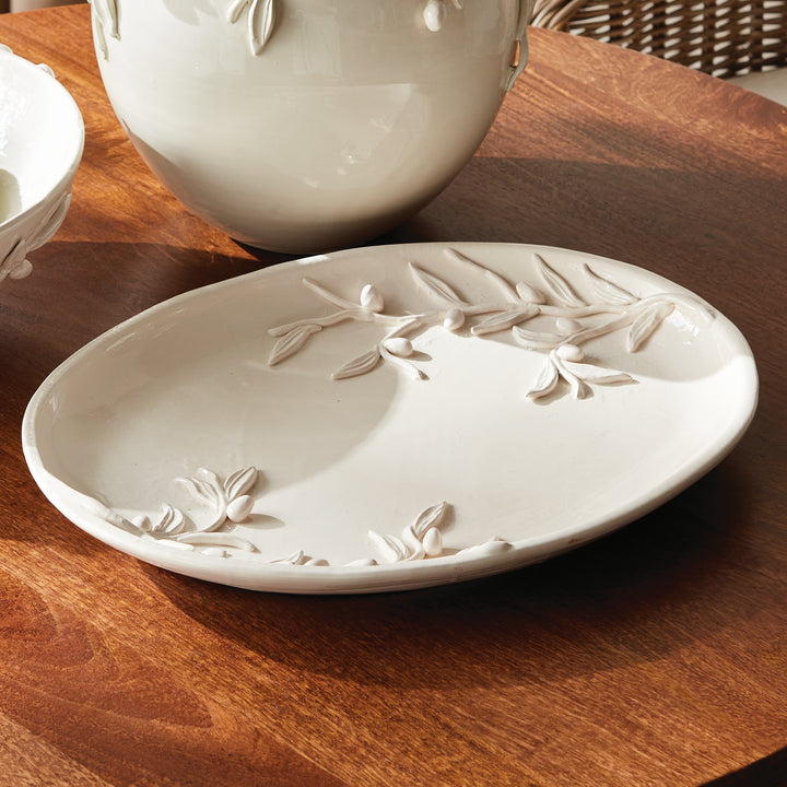 White olive relief tray on a wood table beside the coordinating rounded vase, showing its oval glazed surface. Traditional