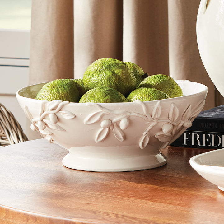 White olive relief footed bowl styled with moss balls on a wood table, showing the rounded base and leaf details. Traditional