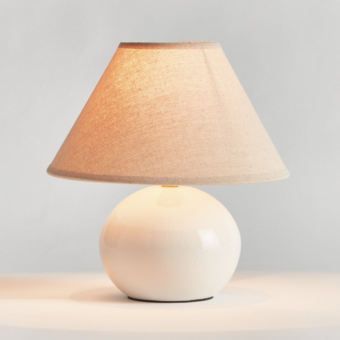 White mini ceramic table lamp illuminated with linen shade glowing softly on tabletop modern accent lighting style