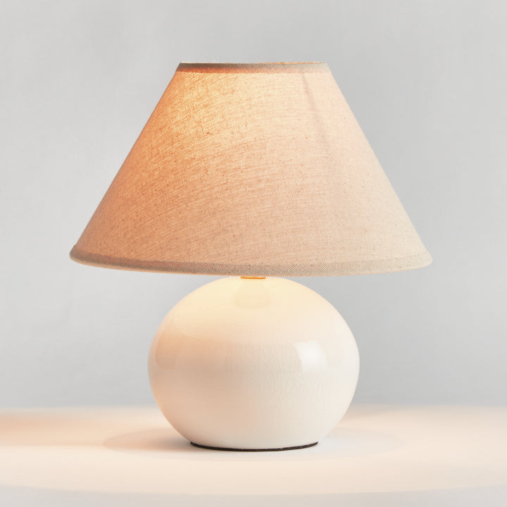 White mini ceramic table lamp illuminated with linen shade glowing softly on tabletop modern accent lighting style
