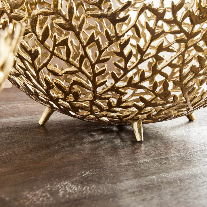 Gold metal bowls with intricate vinework displayed on a dining table with natural light and soft tones.